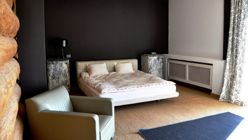 这间卧室采用了鲜明的极简主义风格，黑色的墙壁与空间布局相对立，只有一张低矮的白色床、浅色的扶手椅和一对乡村风格的床头柜。