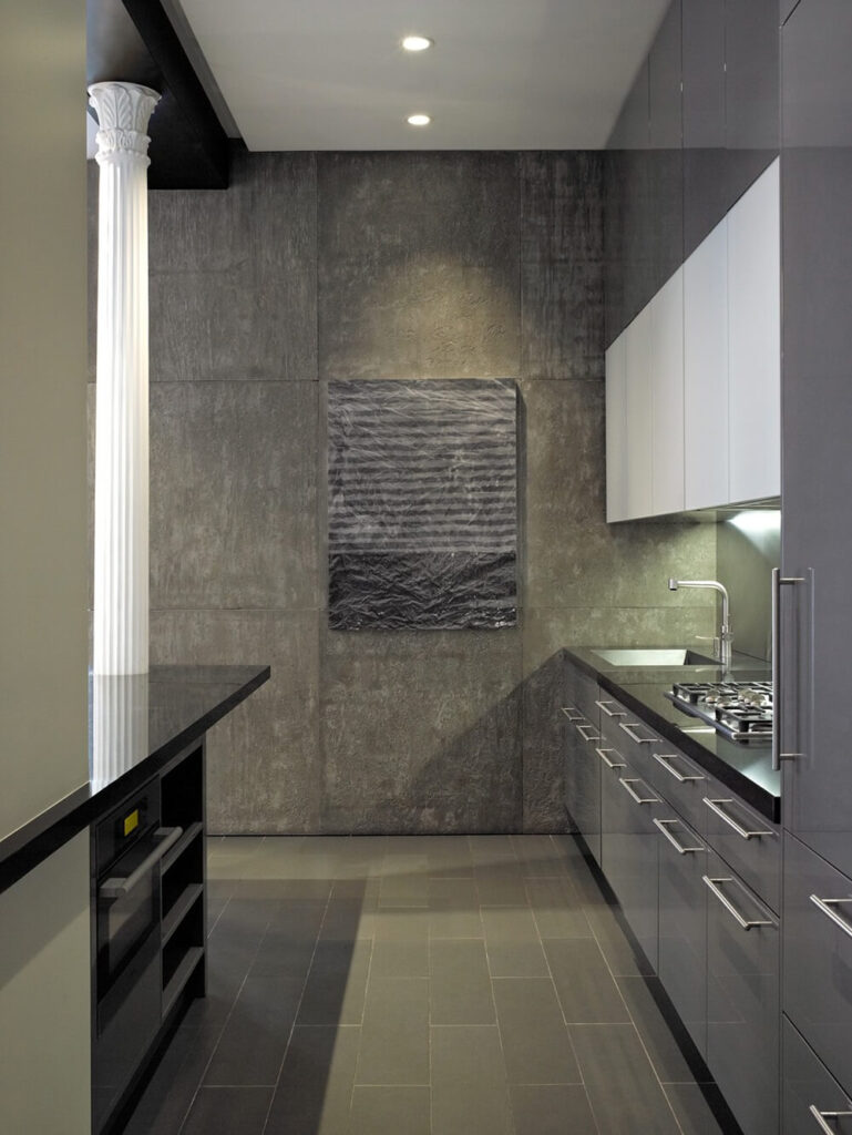 厨房狭长，采用单色配色，配以光滑的不锈钢装饰。墙壁打破了粗糙混凝土的纹理，呈现出脊状和褶皱的外观。