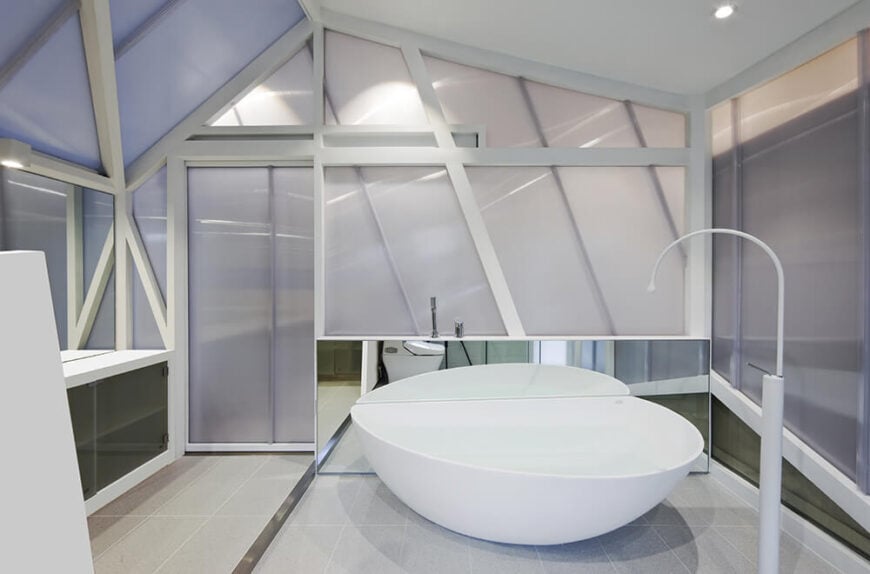 主浴室进一步延续了内部有棱角的、有光泽的外观，中央有一个巨大的白色浴缸，周围是镜面橱柜和烟熏玻璃板。