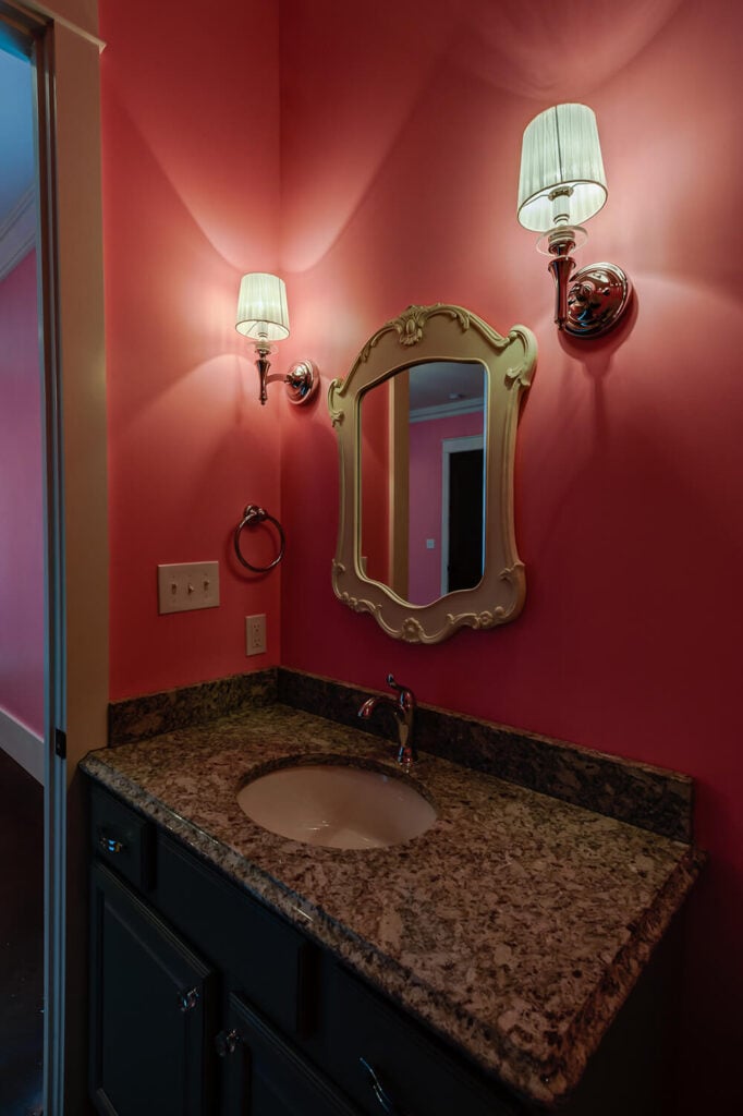 浴室的特色是与卧室相同的亮粉色墙壁。当代的壁灯突出了房间里的银色装置和华丽的镜子。有斑点的花岗岩台面点亮了黑暗的橱柜。