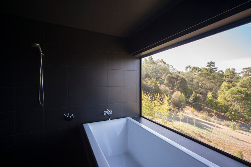 浴室铺满了光滑的黑色瓷砖，以一个巨大的棱角分明的浴缸为中心。右侧巨大的落地窗为在浴缸里放松的人提供了广阔的视野。