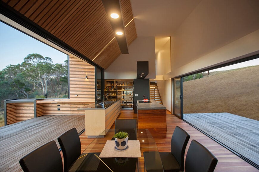 从餐桌的正后方，我们可以看到厨房区域，并可以瞥见通往住宅另一部分的楼梯。岛上丰富的木材纹理与地板很好地匹配，而室内和室外的木镶板与其余空间相呼应。