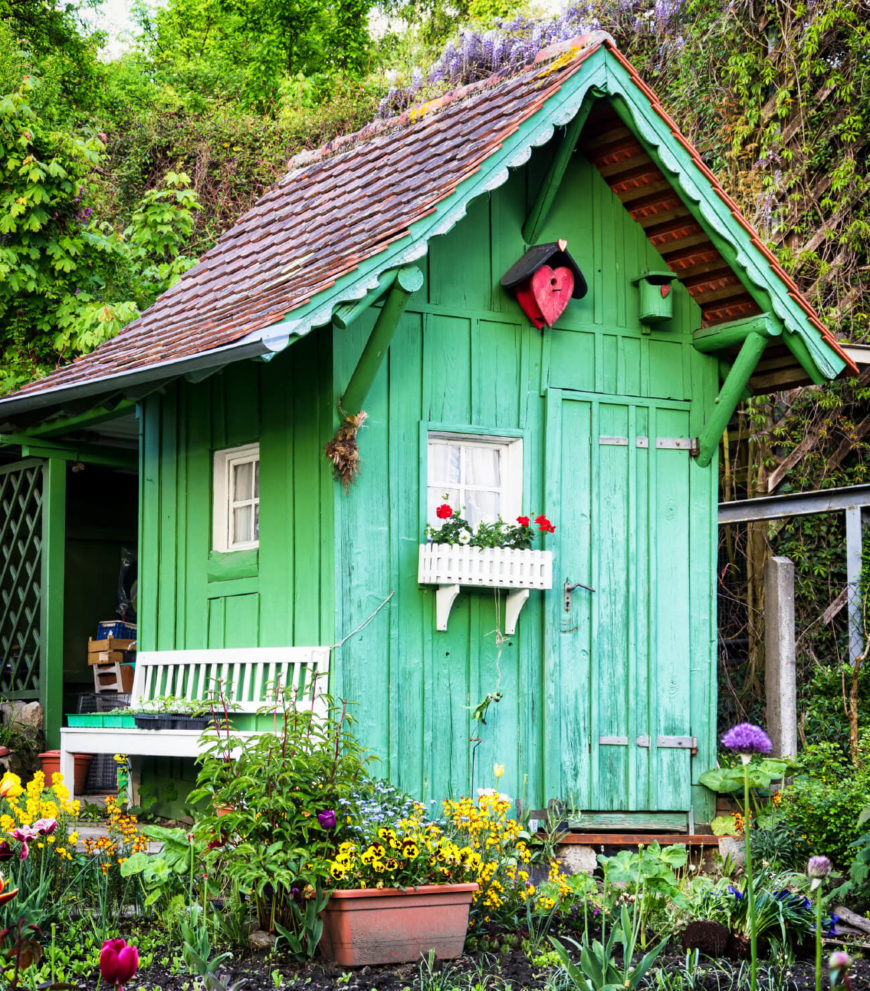 这个明亮的春天绿色小屋有可爱的白色细节和雪松屋顶。它藏在花园的角落里，被色彩和自然美景包围着。