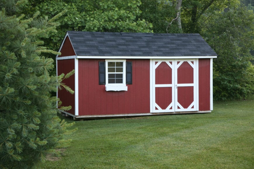 这个漂亮的红色棚屋看起来像一个古老的乡村谷仓，有可爱的百叶窗和黑色的石板屋顶。