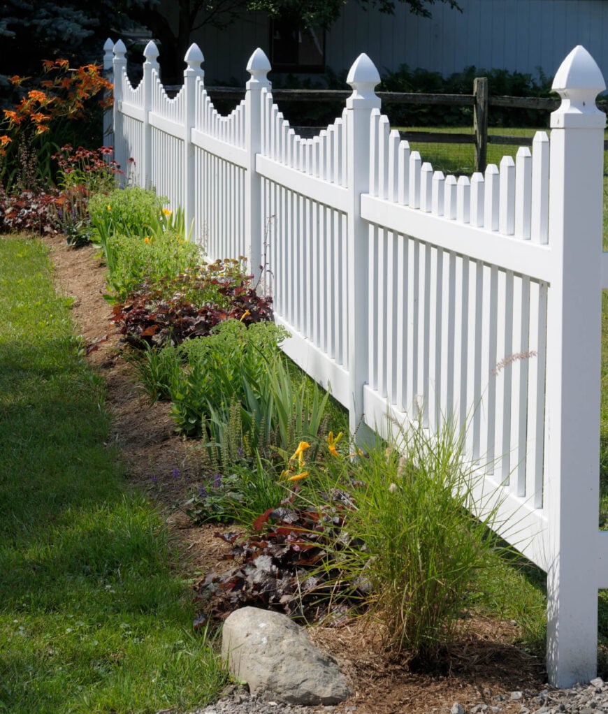 一个可爱的白色乙烯基尖桩栅栏，满足一个分裂的铁路围栏。当围栏主要用于装饰用途时，这可能是省钱的好方法。选择一个不太昂贵的栅栏，在你的栅栏从路上看不到的地方。
