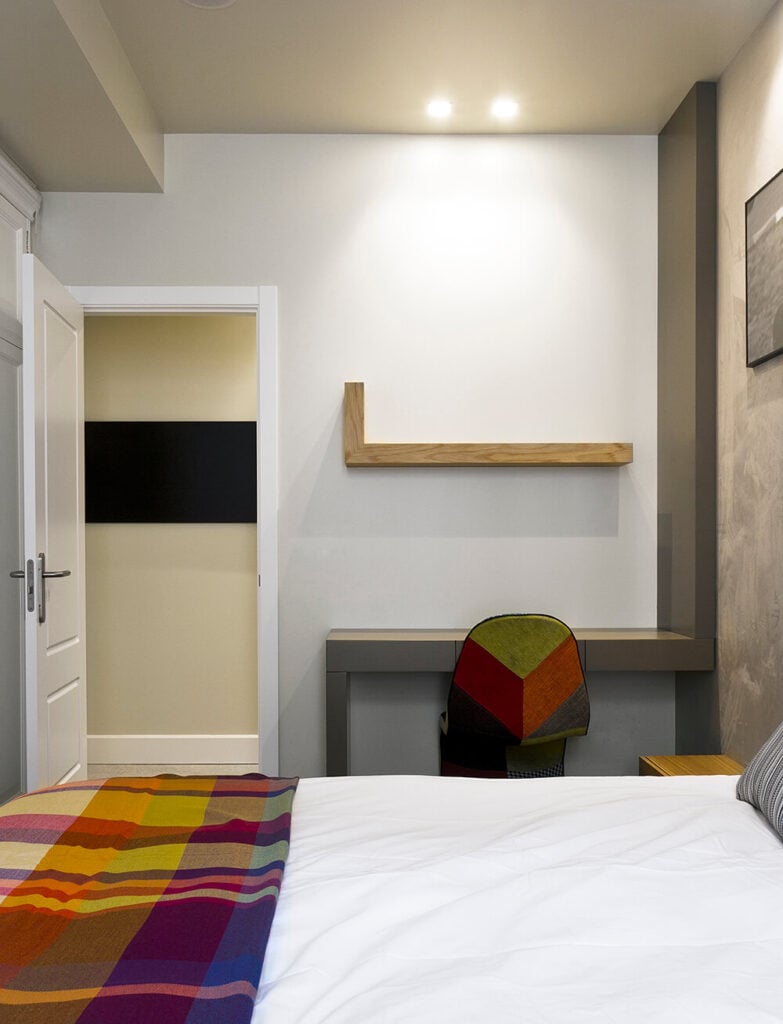 这里是一个孩子的卧室，通过大胆使用彩虹色来区别于主卧室。写字台嵌在墙上，呈棱角分明的灰色色调，上面有一个形状相似的天然木质浮动书架。