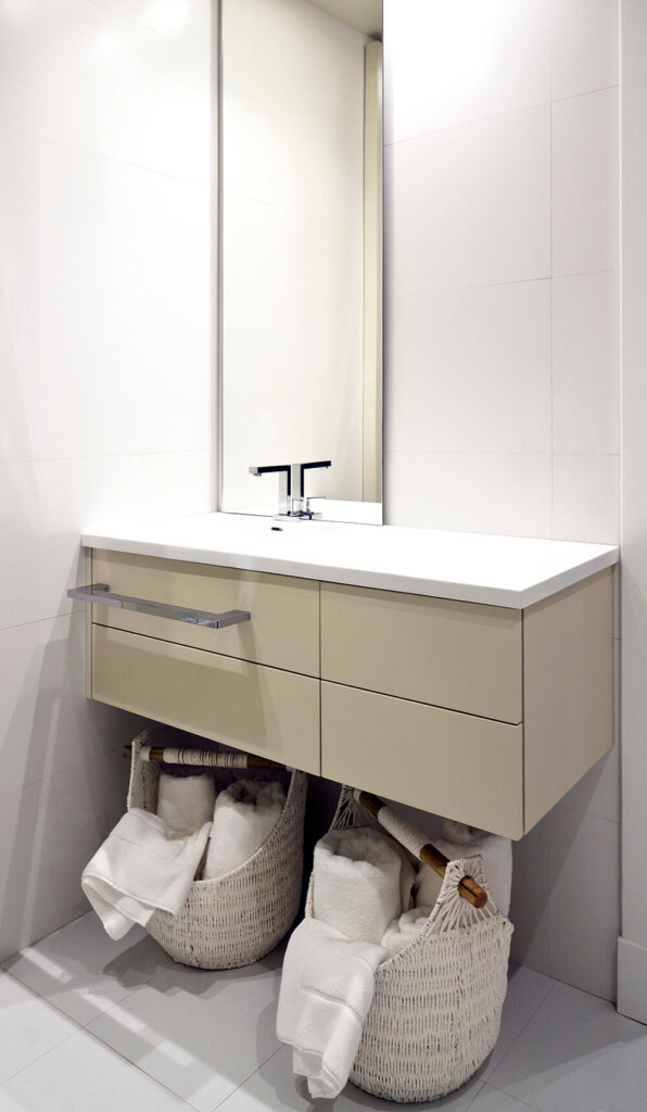 这个浴室以米色和白色的浮动梳妆台为特色，简单的无框镜子沿着上面原始的白色墙壁放置。