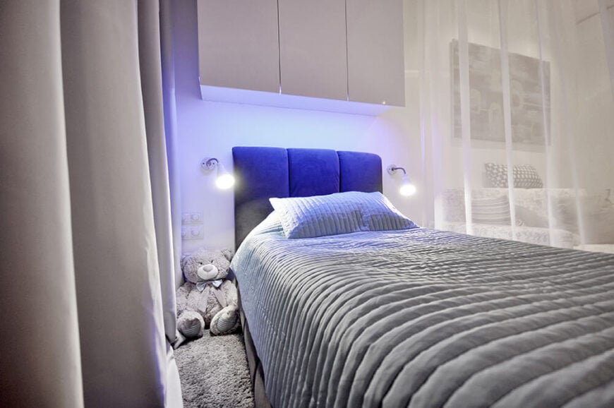 床的特点是一个柔软的蓝色头枕，两侧有一对铰接壁灯。上面是一套光滑的白色橱柜。在左边，我们可以看到所有的照明控制装置，安装在床上任何人都可以触及的地方。