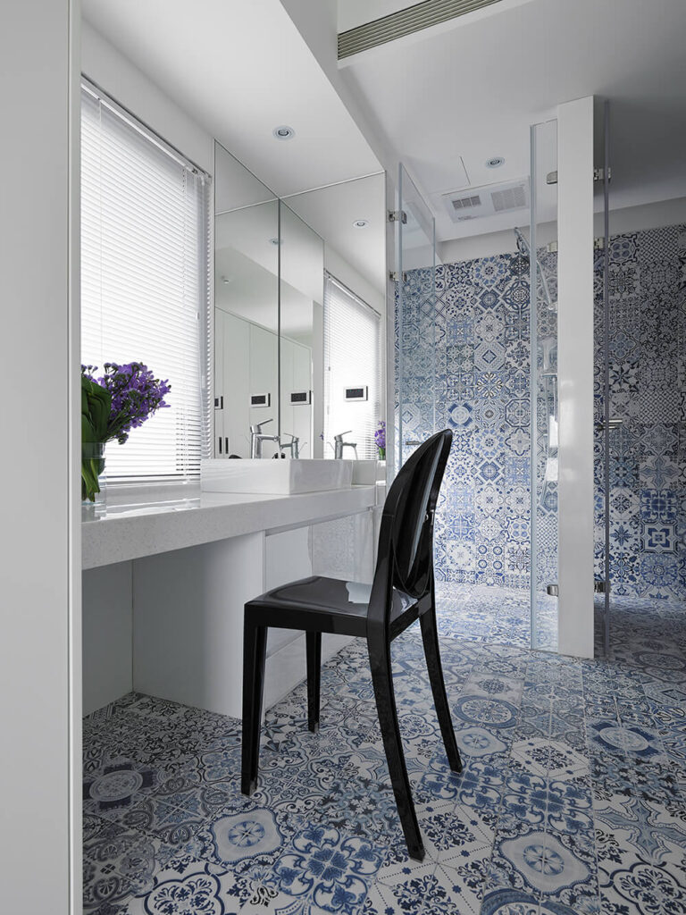 这间浴室配备了步入式淋浴间和大梳妆台空间。白色的墙壁和极简主义的设计与这里复杂图案的蓝色瓷砖形成了对比。