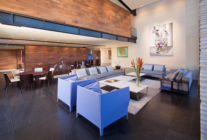 巨大的开放式设计允许像这个集中的客厅和餐厅区这样的巨大空间。深色的石材地板固定了光线和开放空间，与浅色家具和温暖的木镶板形成对比。