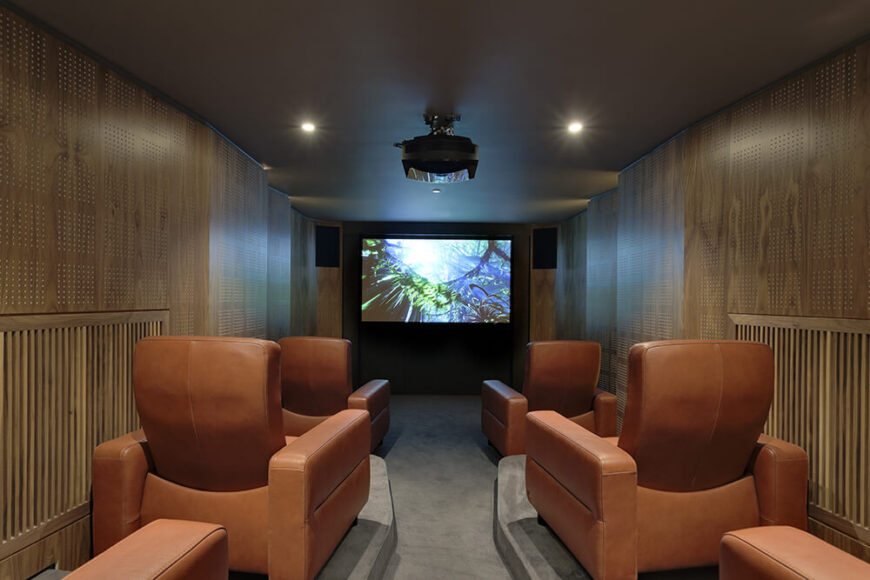 在较低的楼层，我们可以看到更多丰富的木镶板。这是电影放映室，配有专门为观看电影而设计的椅子，还有放映机和远处的大屏幕。