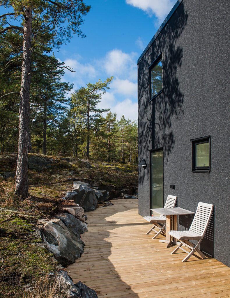 在这张外部照片中，我们可以看到房屋周围的浅色天然木甲板，将其直接置于岩石地形中。高对比度的黑色外观在微妙的景观中脱颖而出。
