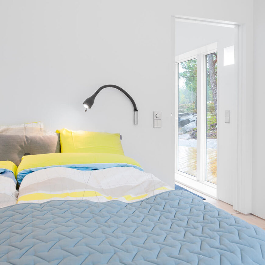 主卧室的特点是色彩的巧妙运用，浅蓝色和黄色的床单与家中其他地方相同的白色墙壁搭配在一起。透过右边的门，我们可以看到通往露台的大型玻璃滑动门。