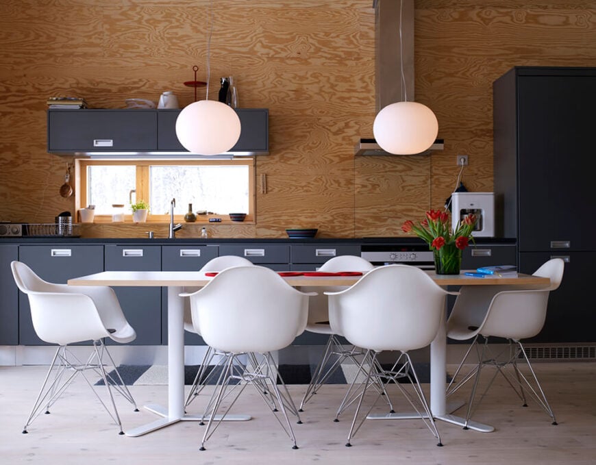 开放式的室内设计让餐厅和厨房的功能在一个广阔的极简空间中重叠。在这里，我们看到温暖的自然木材色调与光滑的深色橱柜和中央的白色大餐桌混合在一起。