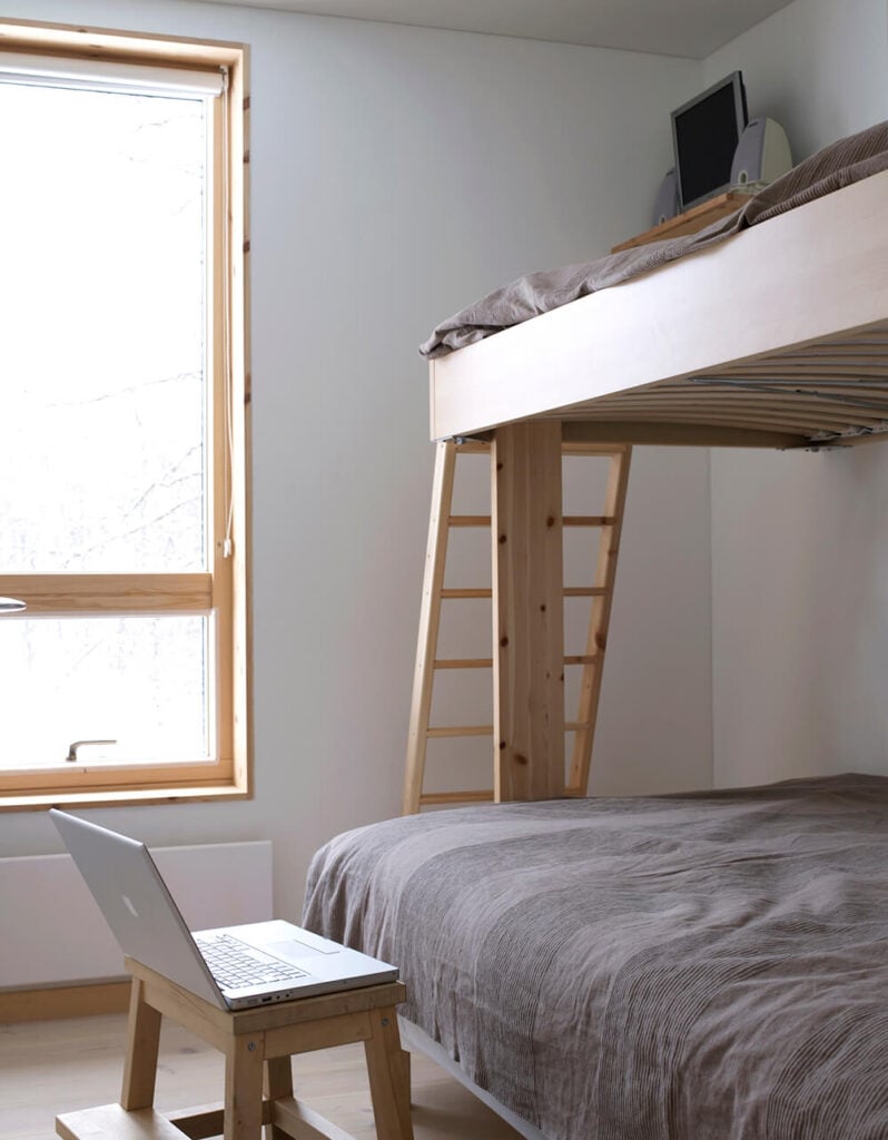 这间卧室采用了节省空间的双层床设计，也采用了丰富的天然木材，与原始的白色墙壁形成了鲜明的对比。极简主义的设置留下了大量的开放空间来活动。