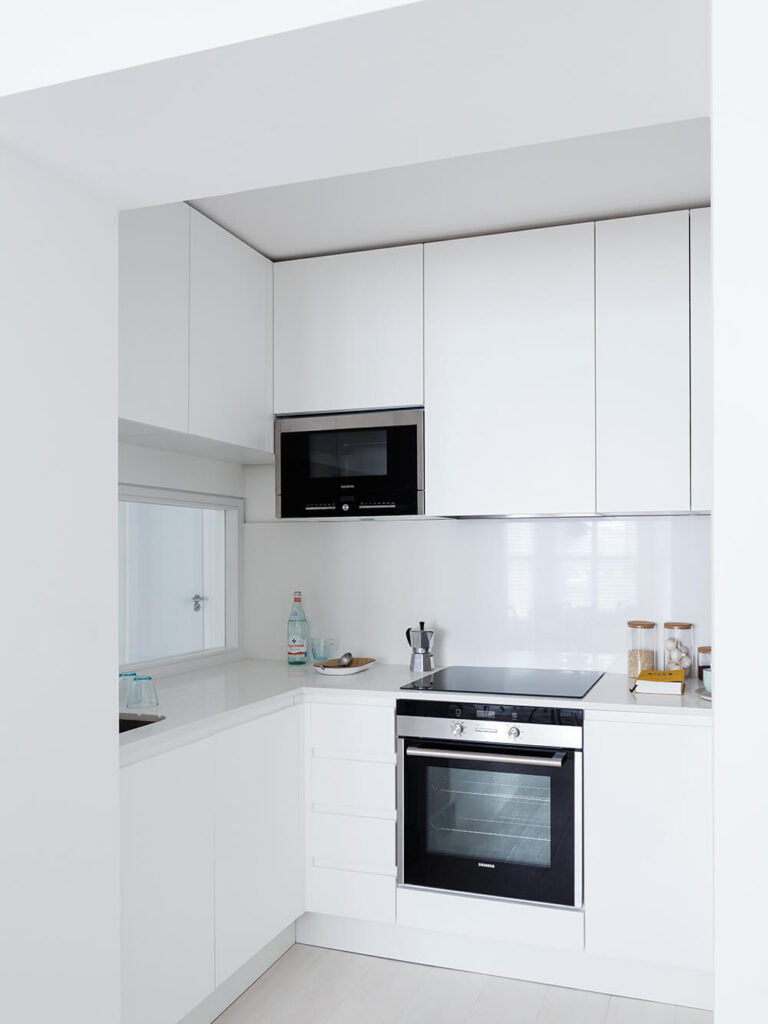 厨房充满了存储选项，得益于光滑的白色橱柜，运行整个空间的高度。极简主义的线条造就了一个引人注目的、独特的房间。
