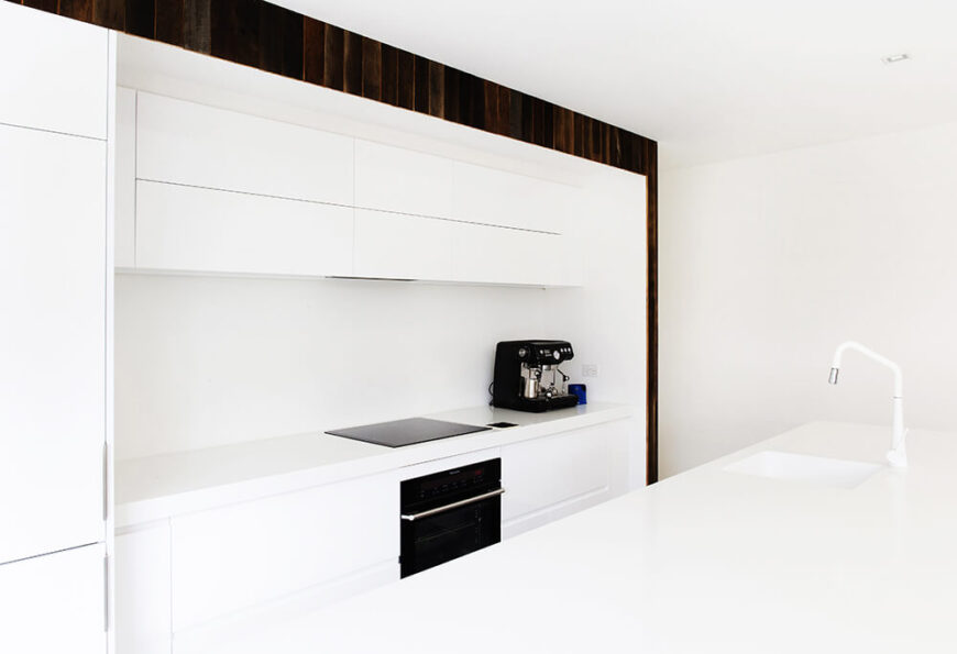 厨房的特点是它的大岛台和全白色，配有光滑的无硬件橱柜和极简主义的电器。天然木板的小边框构成了空间。
