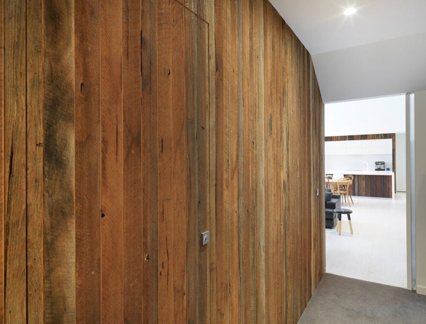 丰富的木镶板延伸到大厅，与家中全白色的开放式部分形成了明显的区别。这堵墙掩盖了一对隐藏的门，只有方形把手的标志。