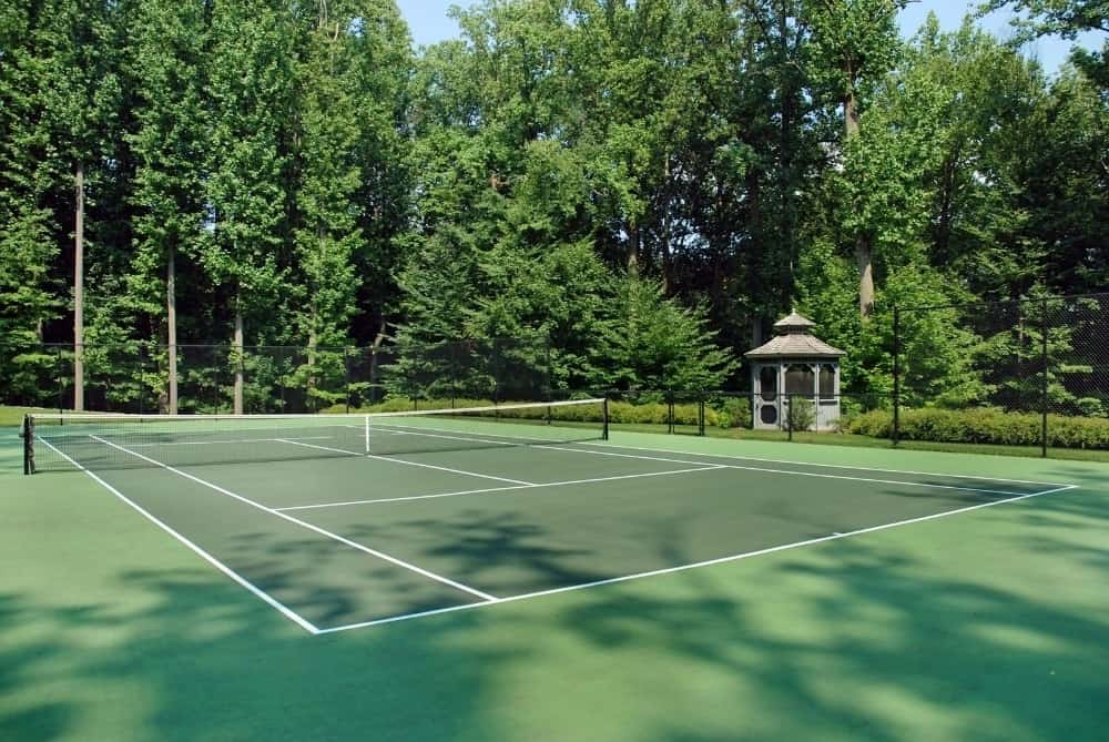 这是该物业的华丽网球场，装饰着高大的松树，与球场的绿色地板相得益彰。图片来自Toptenrealestatedeals.com。