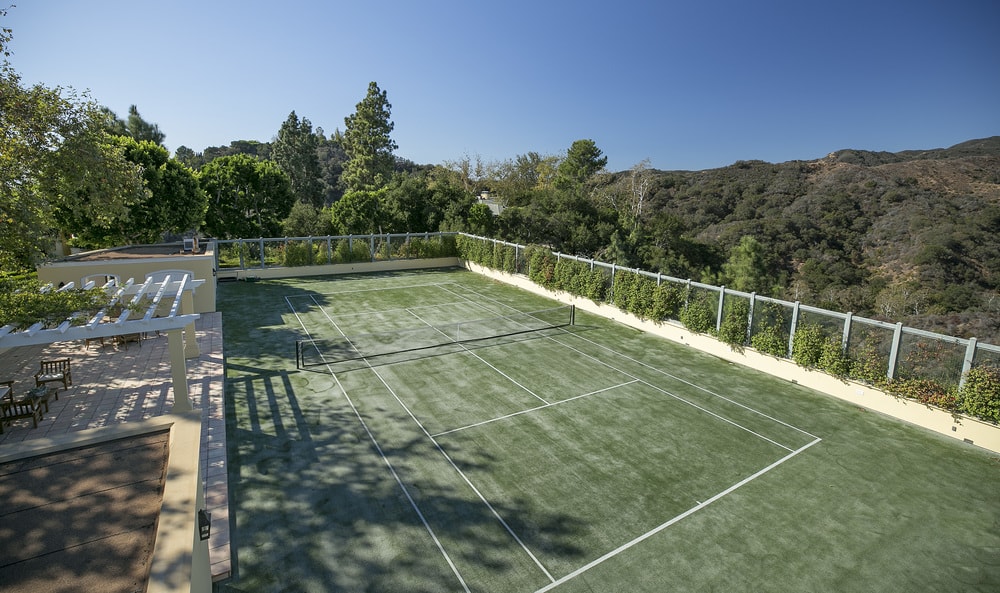 大型室外网球场有绿色的地板，与周围郁郁葱葱的高大树木和灌木相匹配。图片来自Toptenrealestatedeals.com。