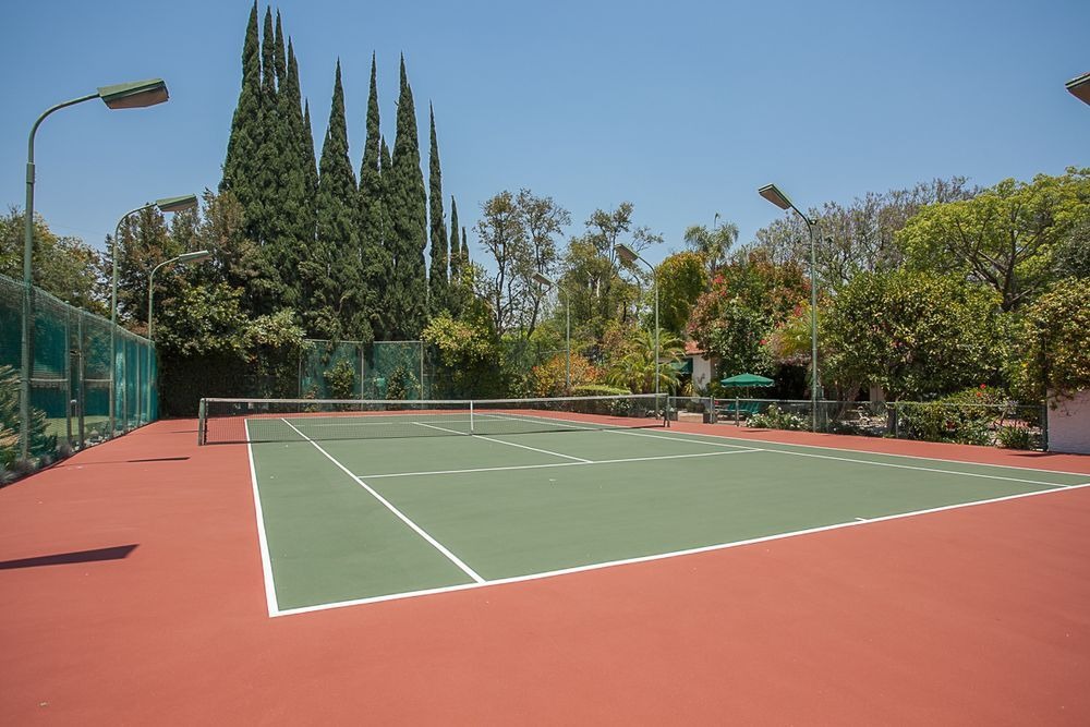 在迷你高尔夫球场一侧设置了一个网球场，周围环绕着茂密的灌木和高大的树木，与球场的陶土色调形成对比。图片来自Toptenrealestatedeals.com。