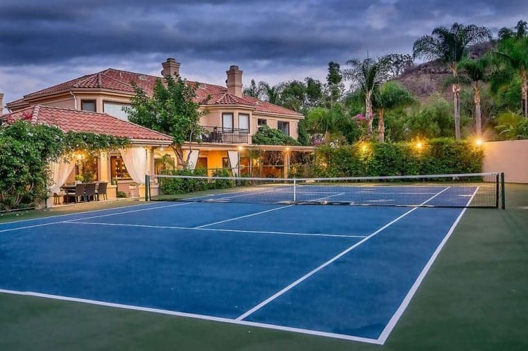这是漂亮的蓝色网球场，就在可爱的家旁边。这里装饰着温暖的室外照明和郁郁葱葱的景观。