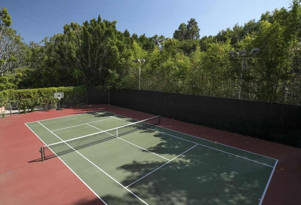 房子的后院有一个完整的网球场。它有高大的栅栏，由匍匐植物和高大成熟的树木装饰，为该地区提供阴凉和魅力。图片来自Toptenrealestatedeals.com。