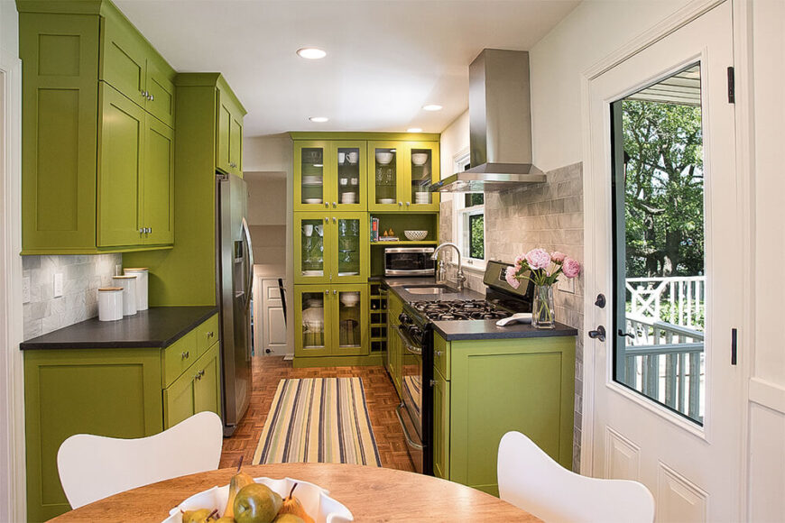 厨房从地板到天花板都采用了大胆的绿色橱柜，具有光滑的表面和少量的玻璃门橱柜。灰色瓷砖后挡板和不锈钢电器完成了现代外观。