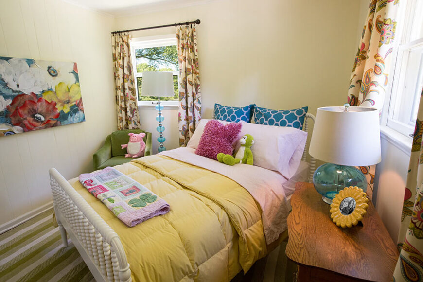 这间为儿童设计的副卧室由花卉色彩、艺术品和其他装饰品装点而成。这个空间还有一对俏皮的蓝色玻璃灯。