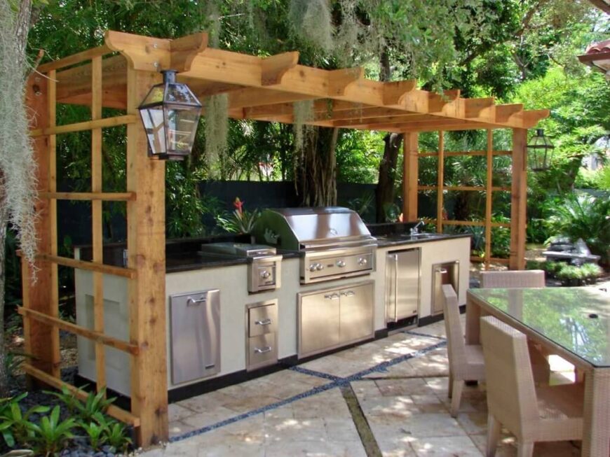 这个凉亭风格的凉亭位于不锈钢烧烤架和室外厨房区域的顶部。这片区域就在大柳树下，柳树的叶子垂在烤架上。