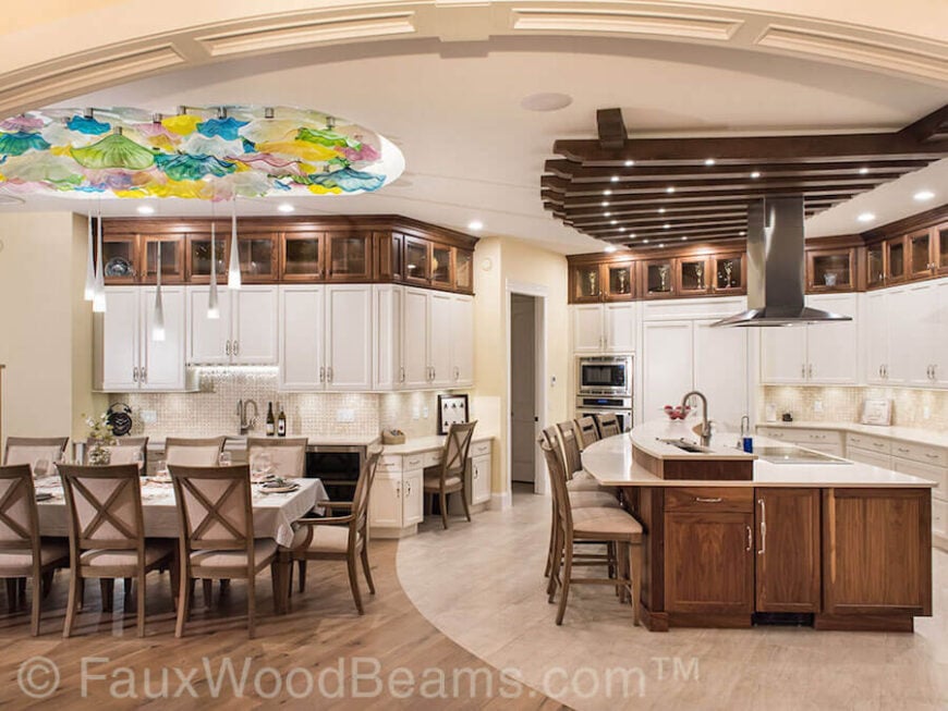 这个美丽的厨房以大量的天然木材为特色，搭配白色橱柜和台面。人造木梁连接在天花板上，呈扇形分布在宽敞的厨房岛台上。