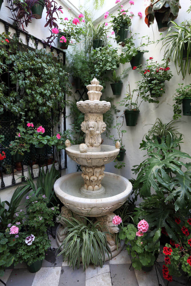 庭院的角落里有无数的盆栽，一个小喷泉和庭院的墙壁上有墙壁花盆。