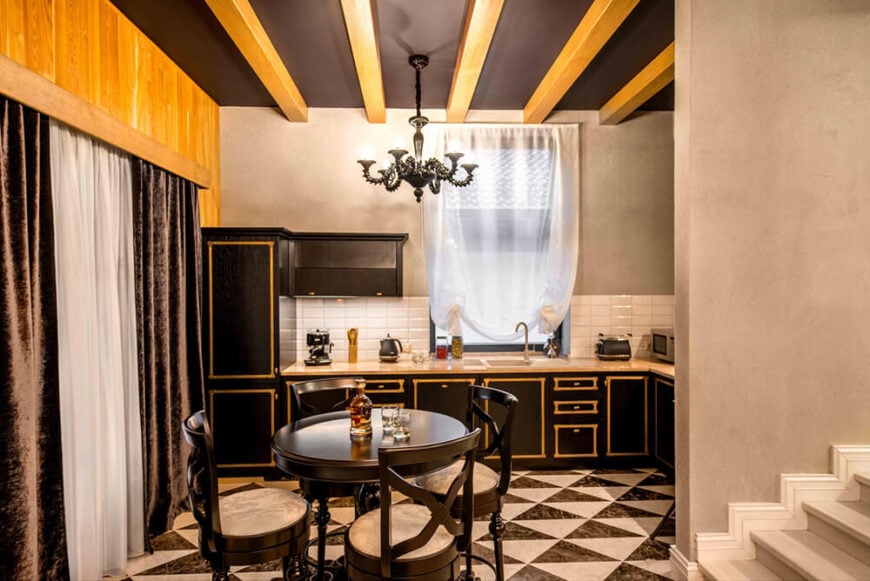 厨房以高度质感的外观脱颖而出，有金色亮点的深色橱柜，格子地砖设计，黑色天花板与天然木材裸露的横梁交叉。