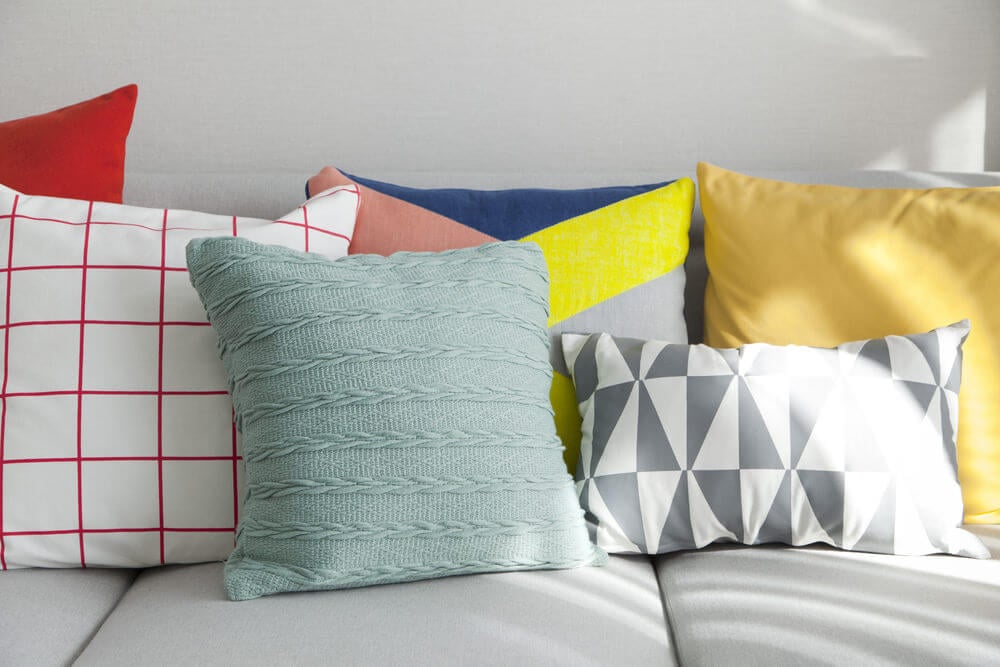 浅灰色的沙发，具有各种各样的掷料枕头 - 坚固的和几何图案以及混合颜色 - 白色，红色，黄色，绿色和灰色。