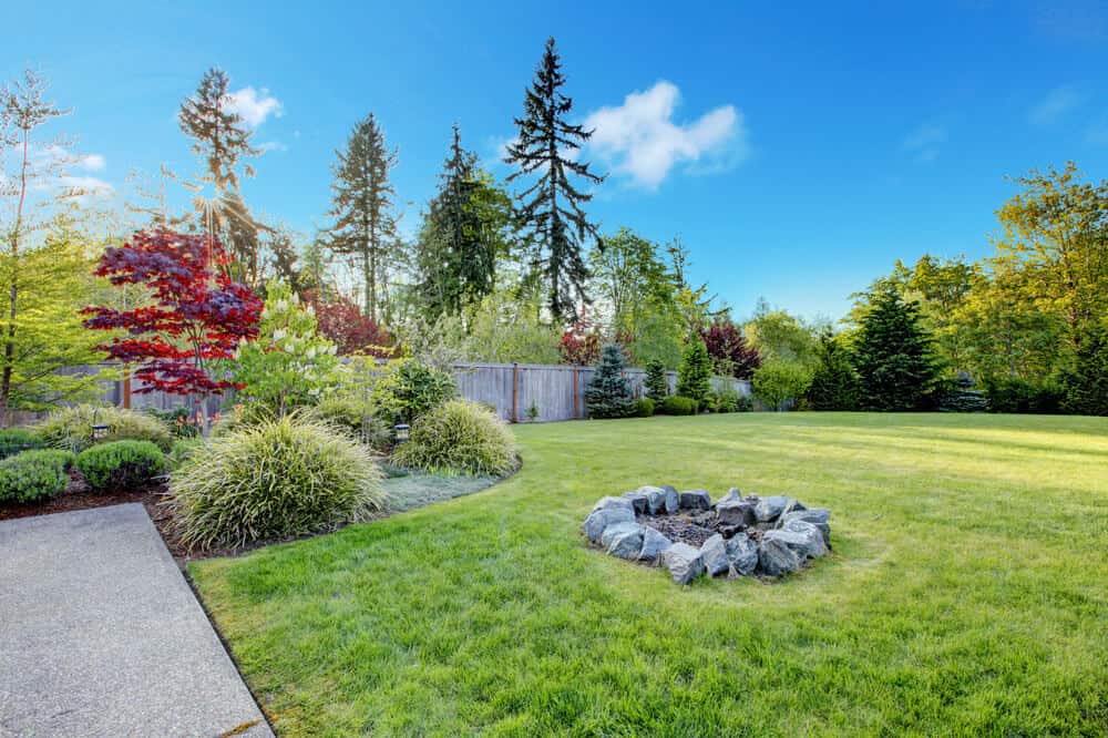 一个有吸引力的简单DIY后院火坑的例子，在一个广阔的草坪中间，用大石头围成一个圈。