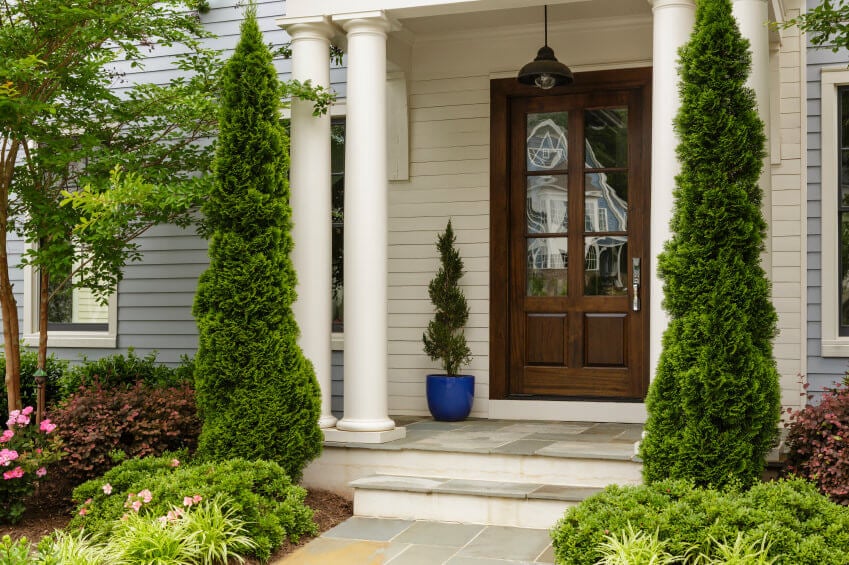 松树柱子自由地矗立在房子的白色柱子旁。你还可以看到在蓝色花盆里种植的螺旋形修剪植物。