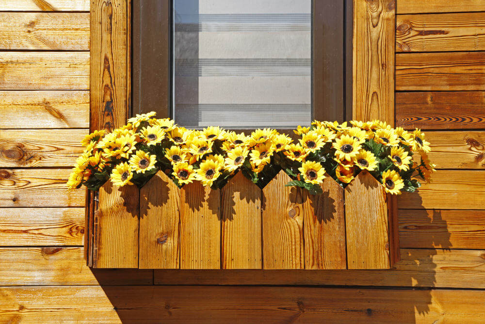 定制的木质花盒，与外部住宅的木材相同，放置在装满黄色花朵的窗户下。