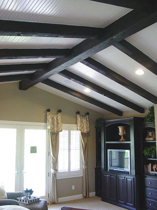 深色的人造木梁与客厅的娱乐中心相匹配，与有质感的白色天花板形成了鲜明的对比。
