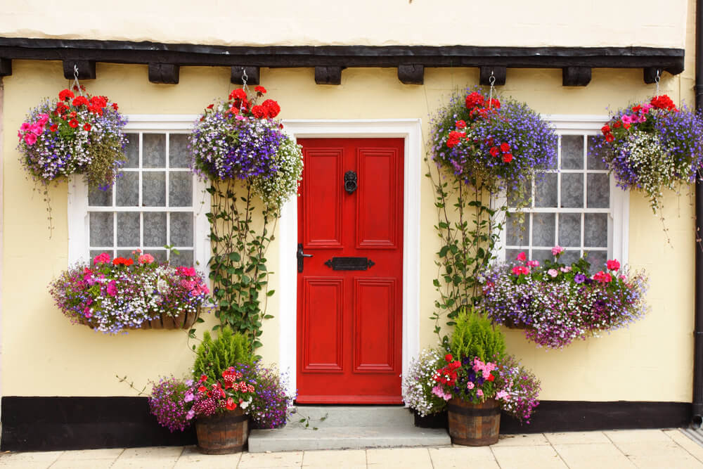 欧洲一所老房子的正面façade，红色的门两侧有白色的框窗，下面有华丽的花盒。