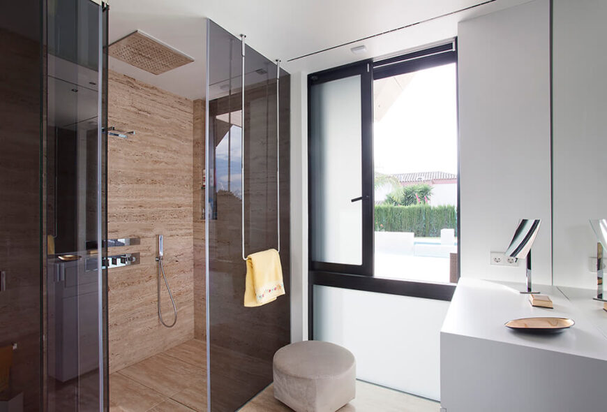 黑色玻璃和大理石图案延伸到浴室，淋浴间周围环绕着有色玻璃和纯白色的台面和墙壁。单色主题被淋浴瓷砖打破了一点，但它作为整体设计的重点。