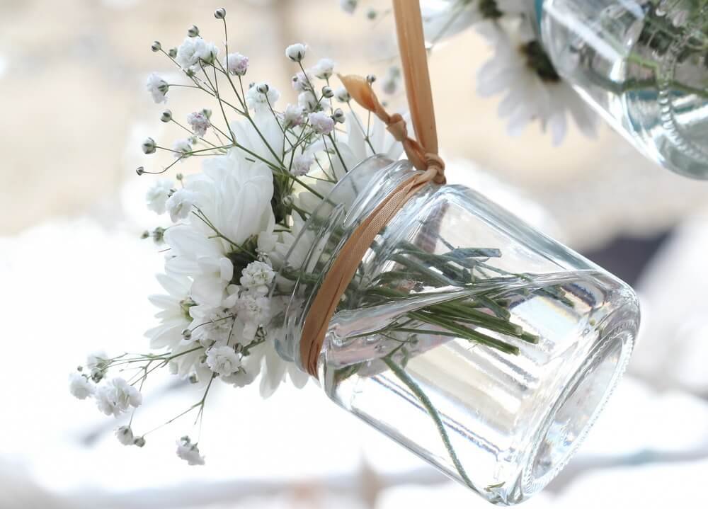 一个清晰的梅森罐用于一个小的白色花束的图片。这可以用来装饰一个户外空间，使用许多他们，例如，周围或上面的庭院空间。