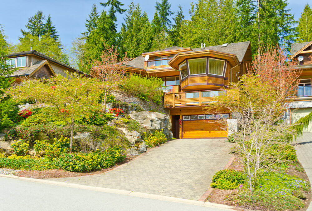 一种木房子建筑设计，坐落在斜坡上，旁边是一个巨大的岩层，树木和其他绿色植物在那里生长和发芽。