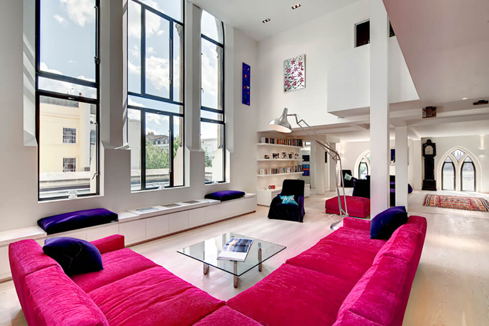 在伦敦DOS Architects设计的住宅中，客厅有一个巨大的开放空间，有一面墙的窗户，可以吸收大量的自然光。一个大的亮粉色沙发定义了座位区，窗户下有一个长板凳。房间还包括一个书柜，嵌入式照明，一个玻璃面咖啡桌，强调椅和一个与沙发相匹配的热粉色软脚凳。