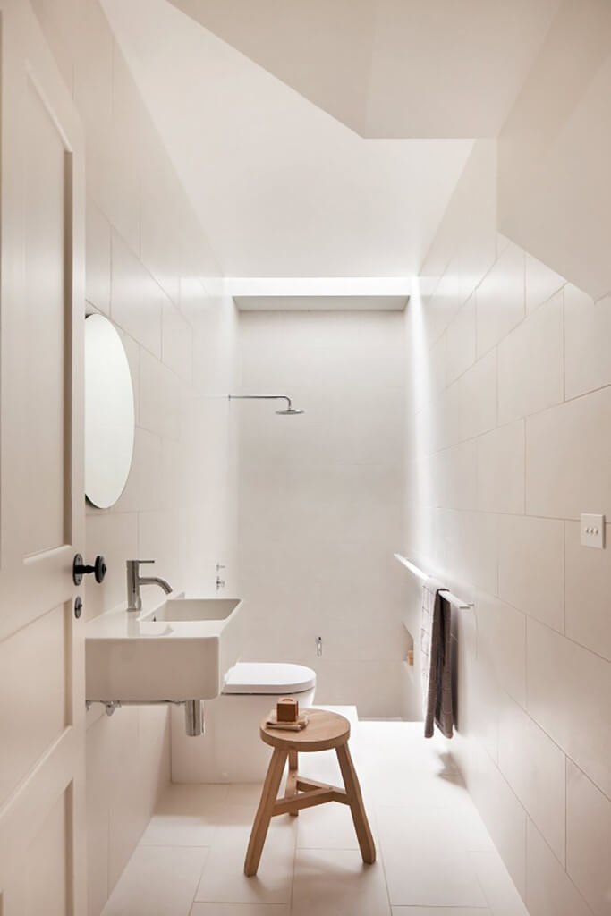 浴室贴满了白色的大面积瓷砖，从地板往上都是。一个简单的浮动梳妆台挂在步入式淋浴间附近，中间没有分隔。