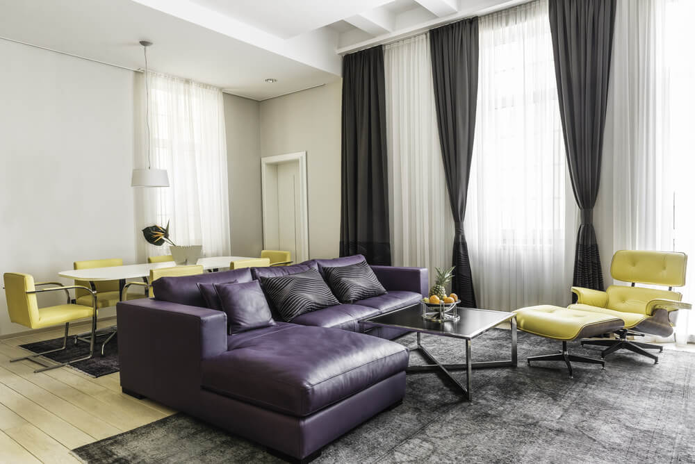 这个起居空间的特色是紫色的l型沙发，中间的桌子放在灰色地毯上，上面覆盖着硬木地板。