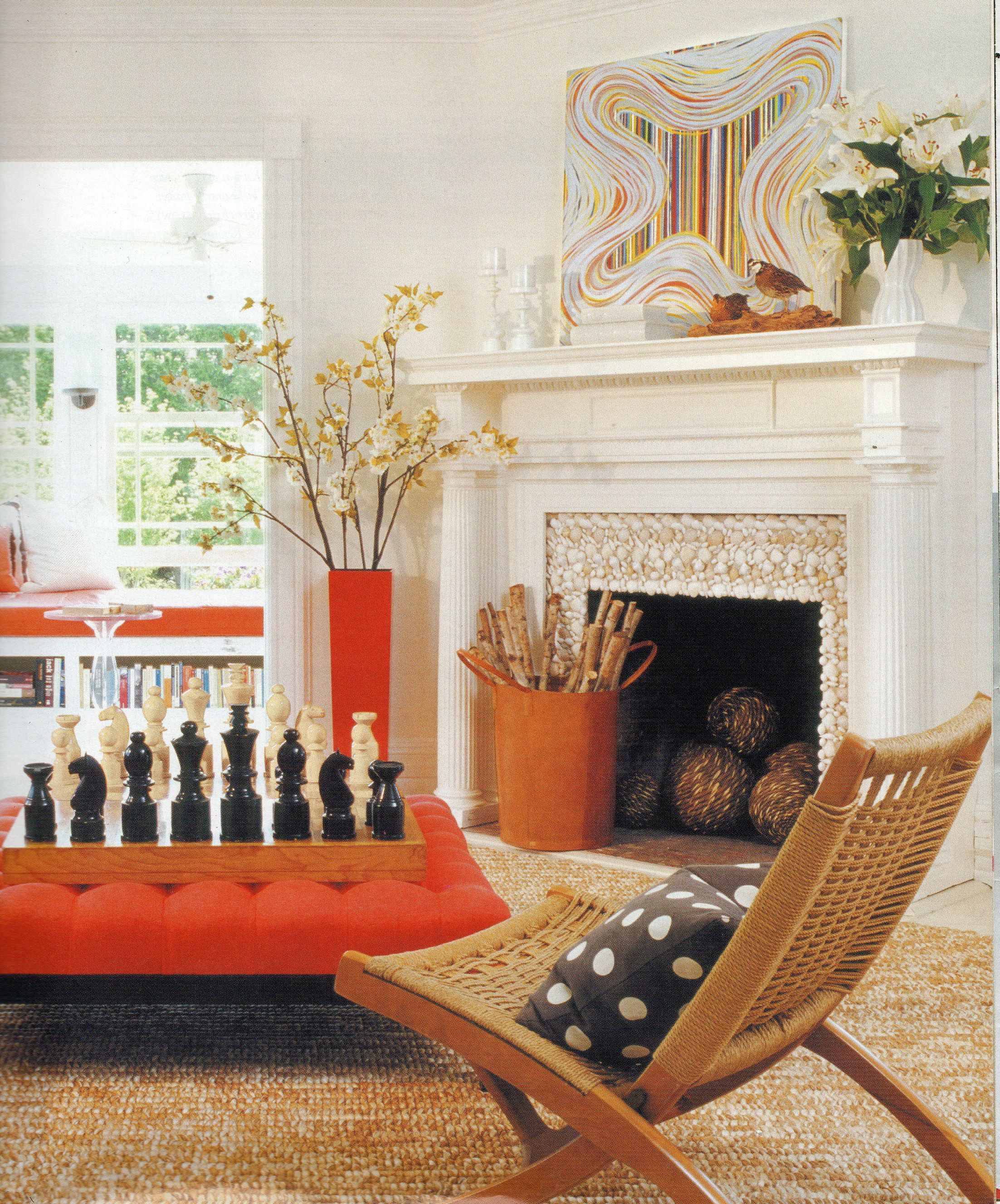这个客厅的精致色彩选择脱离了常见的客厅配色方案，加入了橙色。摆放着棋盘和超大棋子的中央搁脚凳、花瓶、窗凳、柴火架和艺术品都引人注目。