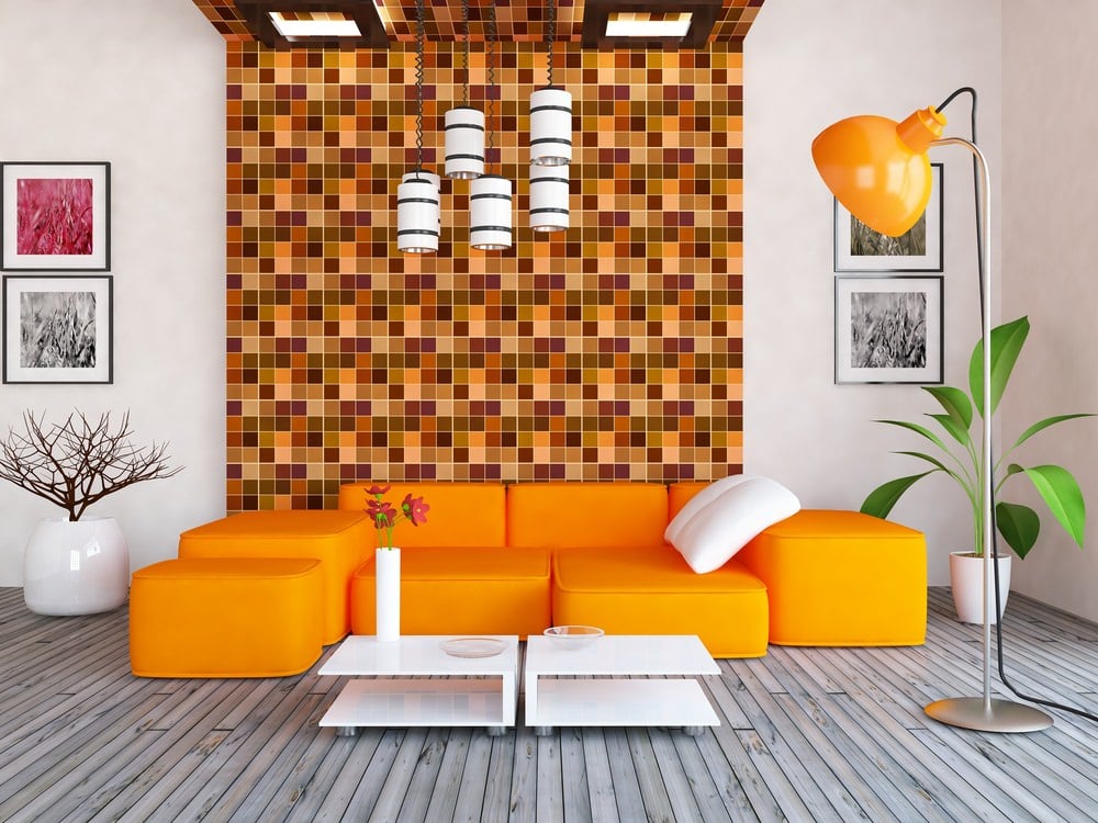 强调墙上不同调色板上的橙色图案开玩笑地将浅橙色和深橙色并列排列在小方块中。这种橙色设计的几何感也与沙发套装完美搭配，而橙色落地灯则展示了自己的阴影。