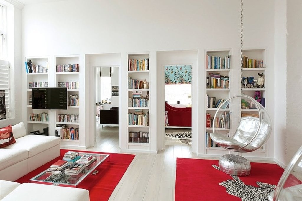 白色的沙发、书架、墙壁、地板和天花板被带有豹纹的红色地毯突出。这把时髦的圆形挂椅上银色的靠垫闪闪发光。
