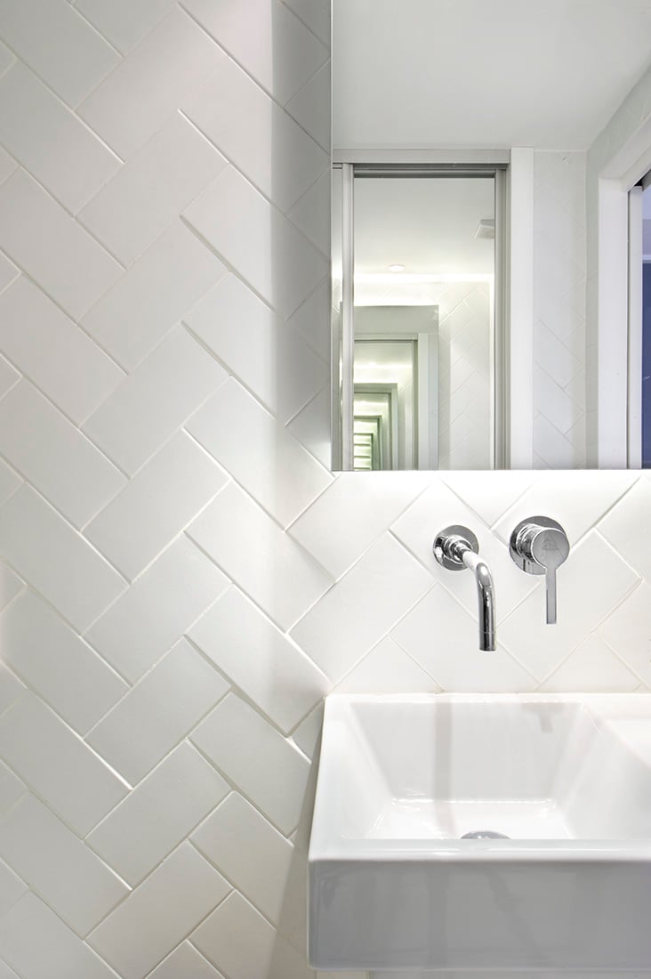 人字型白色瓷砖，水槽和水龙头，使这个浴室的功能和美观的设置完整。加上镜子，在空间上创造一个更大的错觉。