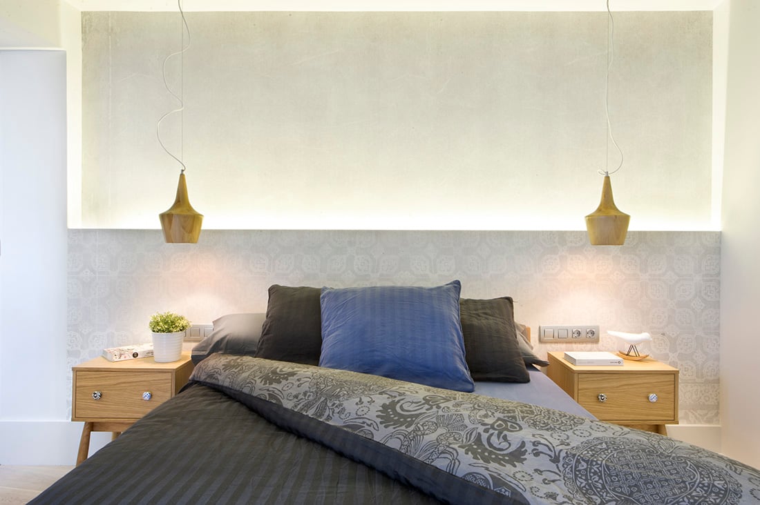 对称的插头、桌子和悬停在天花板上的吸顶灯。额外的照明被提供在有图案的墙后面，也作为艺术的床头板。